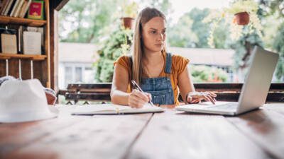 Student taking notes in a notebook while on a laptop researching prestigious colleges